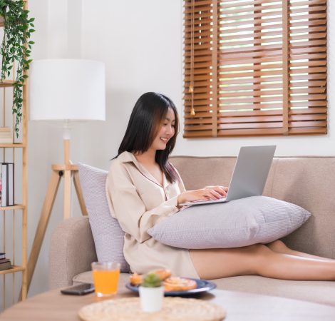 Concept of activity in living room, Young Asian woman use laptop to surfing social media on sofa.